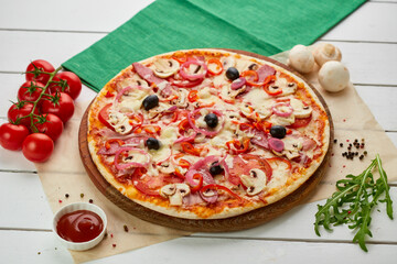 Freshly baked pizza with smoked sausages, red pepper, mushrooms, onion and olives served on wooden background with tomatoes, sauce and herbs. Food delivery concept. Restaurant menu