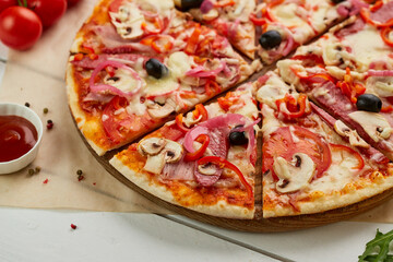 Freshly baked pizza with smoked sausages, red pepper, mushrooms, onion and olives served on wooden background with tomatoes, sauce and herbs. Food delivery concept. Restaurant menu