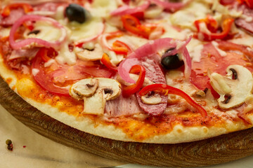 Freshly baked pizza with smoked sausages, red pepper, mushrooms, onion and olives served on wooden background with tomatoes, sauce and herbs. Food delivery concept. Restaurant menu