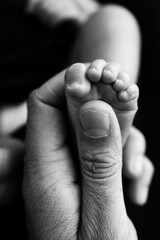 Close up baby feet in mother hands on a black background. Prevention of flat feet, development, muscle tone, dysplasia.Mother is doing massage on her baby foot.Black and white photo. 