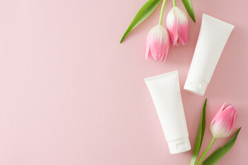 Organic cosmetic idea. Top view photo of white cosmetic tubes without label and pink tulips on isolated pastel pink background with copy space