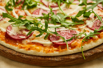 Freshly baked tasty pepperoni pizza with salami, mozzarella cheese and rukkola served on wooden background with tomatoes, sauce and herbs. Food delivery concept. Restaurant menu