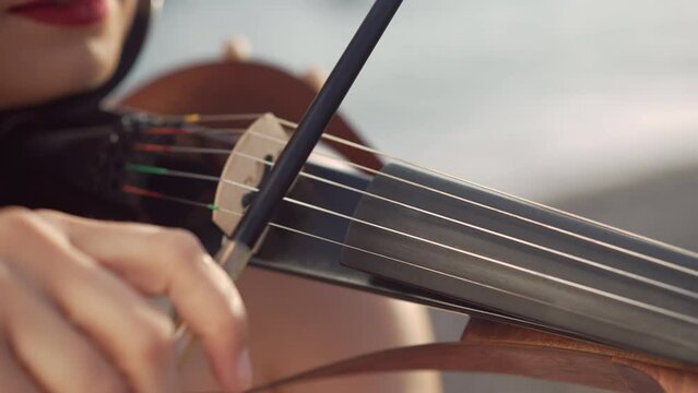 Close-up violin bow in female hands playing strings of musical instrument outdoors. Unrecognizable Caucasian talented lady enjoying music in sunshine