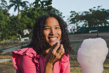 Beautiful afro hispanic girl having fun in the park and eating cotton candy. Happy black woman smiling in the park, Lifestyle. Concept of people and happiness. 