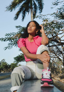 Relaxed young african latina woman wearing fashion colors with afro hair sitting on street, mixed race girl generation z, hipster lady posing on outdoor background.