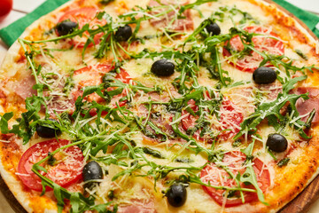Freshly baked pizza with ham, rukkola, sauce pesto and olives served on wooden background with tomatoes, sauces and herbs. Food delivery concept. Restaurant menu