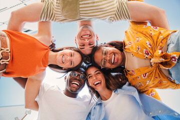 low view angle of a group of multiracial teenagers smiling and looking at camera together. Portrait of five young students smiling and laughing. Cheerful people having fun and embracing each others