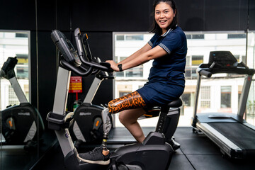 Young woman with prosthetic legs and workout clothes doing exercises on a treadmill on a bicycle in...
