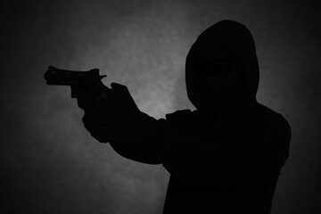Mysterious man wearing black hoodie holding a pistol, shooting with a gun. Silhouette and dark concept image