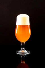Glass goblet with light lager beer, on a glass black table, black background.