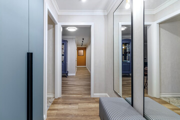 View of the long corridor in the modern apartment from the hallway with large mirrors and wardrobe