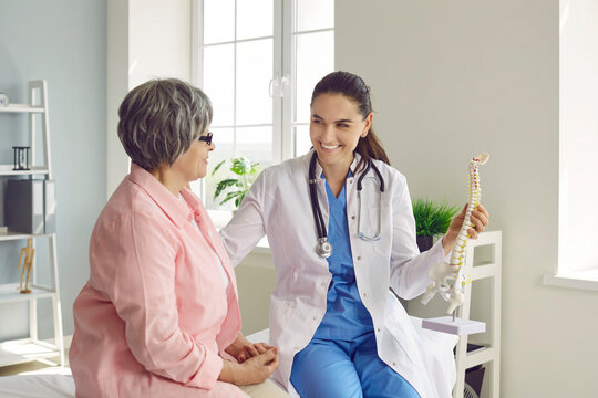 Doctor showing spine model to senior woman patient. Friendly, smiling medical specialist talking to old lady, telling about skeleton diseases, and showing orthopedic anatomical backbone model