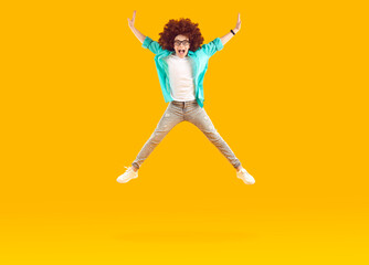 Happy child jumping and having fun. Funny cheerful energetic little boy in casual clothes and curly wig jumps up and flies in mid air on amber yellow orange background. Children, fun, energy concept