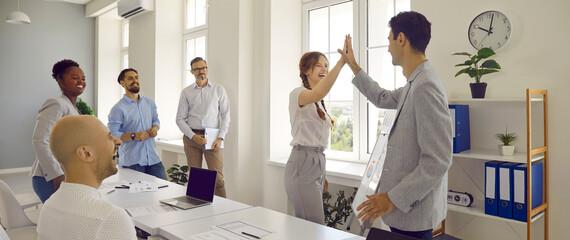 Work success. Joyful colleagues give each other high five in office after successfully completed work together. Male and female worker succeed together at business meeting in office. Web banner. © Studio Romantic