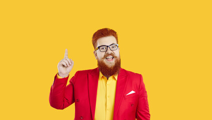 Fototapeta premium Portrait of funny joyful and excited chubby bearded man who came up with great idea. Joyful caucasian redhead fat man in red jacket and glasses raises index finger up looking at camera with open mouth