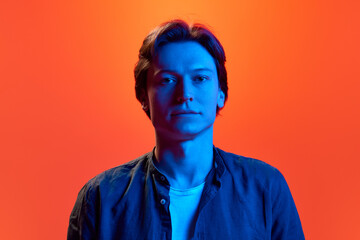 Portrait of young man, guy with calm face looking away over red-orange background in neon light. Concept of beauty, youth, human emotions, mood, ad