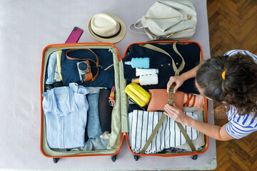 Top view of young woman packing suitcase for travel - Powered by Adobe