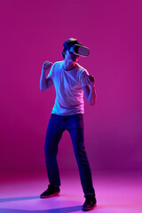 One young boy wearing VR glasses over pink background in neon light. Youth and virtual lifestyle of future. Gaming addiction