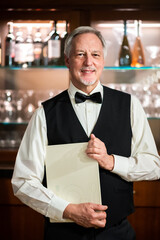 Portrait of a senor maitre in an elegant restaurant holding a couple of menus