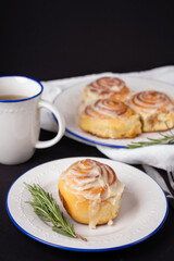 homemade cinnamon rolls on white ceramic plates decorated with rosemary and a cup of tea