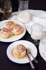 cinnamon rolls on white plate with blue rim decorated with rosemary and jug of milk