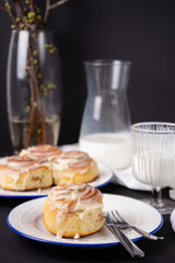 cinnamon rolls on white plate with blue rim decorated with rosemary and jug of milk