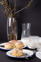 cinnamon rolls on white plate with blue rim decorated with rosemary and jug of milk