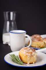 homemade cinnamon rolls on white ceramic plates decorated with rosemary and a cup of tea