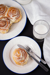 cinnamon rolls on white plate with blue rim decorated with rosemary and a glass of milk
