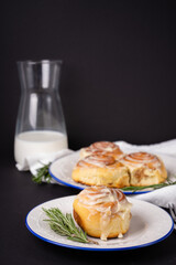 cinnamon rolls on white plate with blue rim decorated with rosemary and jug of milk