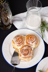 cinnamon rolls on white plate with blue rim decorated with rosemary and jug of milk