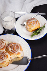 cinnamon rolls on white plate with blue rim decorated with rosemary and glass of milk