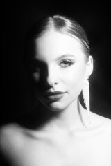 Fototapeta premium Beauty, make-up and fashion concept. Beautiful classic woman studio portrait. Model with classic hairstyle and fancy earrings. Shiny star filter applied. Model looking at camera. Black and white image
