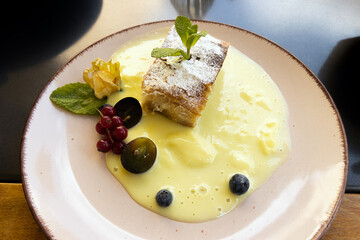 Appetitlich mit Minze und Früchten angerichteter Apfelstrudel mit Vanillesauce.