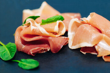 Pieces of dried pork jamon prosciutto on a black board.