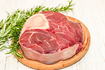 Fresh piece of meat large beef steak on the bone ossobuco with rosemary sprig.