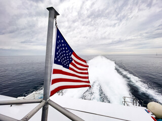 Ultra wide shot of American flag flapping in the wind on the back of a fast boat in the ocean with wake stretching backwards