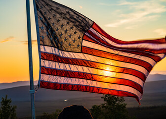 Beautifully backlit American flag blows in the wind and covers up the sun setting behind it