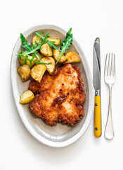 Chicken milanese with crispy potatoes and rocket salad jy the light background top view