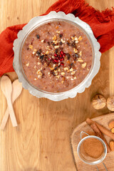 Top view photo of a bowl of a traditional Turkish dessert ashure, Noah's Pudding. Dessert decorated with pomegranate seeds, nuts, and a sprinkle of cinnamon powder, along with dried figs on the side. 