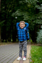 Fototapeta premium Boy of school age with a blue backpack goes to school in the park