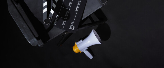 Black director chair and black clapper board on chair and megaphone on black background. Top view.