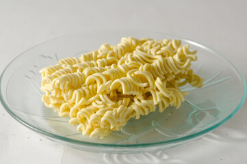 Uncooked instant noodles cut in half on a small plate isolated on a white background