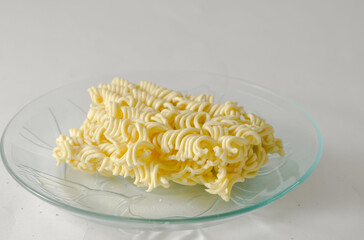 Uncooked instant noodles cut in half on a small plate isolated on a white background.