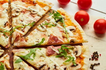 Sliced Freshly baked pizza with ham, rukkola and mushrooms served on wooden background with tomatoes, sauces and herbs. Food delivery concept. Restaurant menu