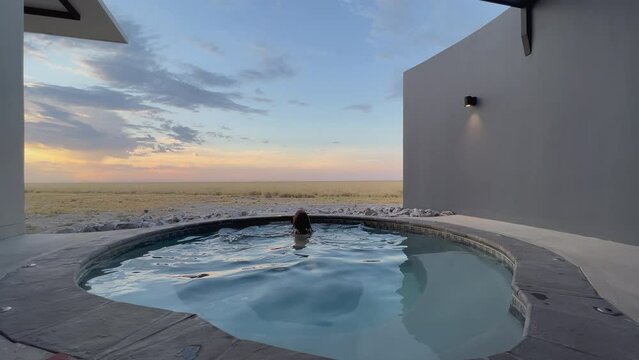 A young woman in a beige bikini enters a private swimming pool.
