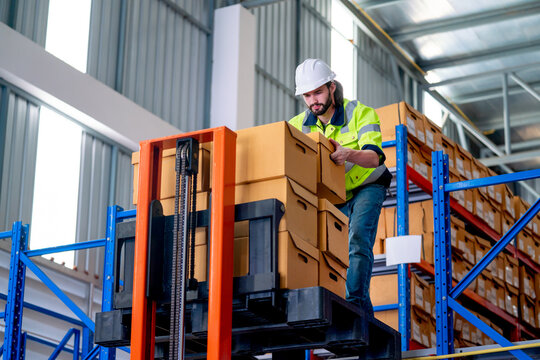 Professional warehouse worker man hold and carry box out from cargo truck that lift up the state for the man on upper level in workplace.