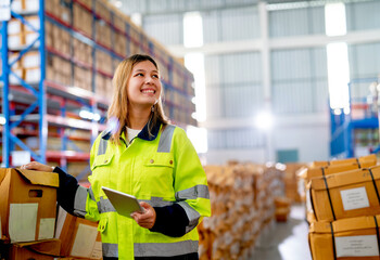 Beautiful young warehouse worker woman hold tablet and smiling also look to her left side in...