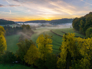 Aerial drone Sunrise view Above autumn colored forest and Valleys in Luxembourg, covered in morning fog