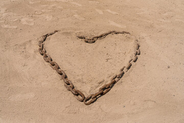 Links of rusty iron chain in the shape of a heart in the sand of a beach